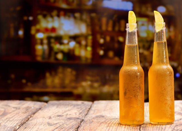 2 bottles are shown on a table with a bar scene in the background