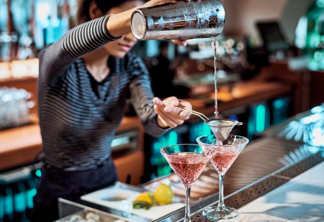 preparation of a cocktail is shown in the foreground with a beautifully illuminated Gamko cabinet shown in the background.