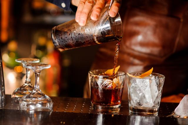 a bartender pours a cocktail over ice