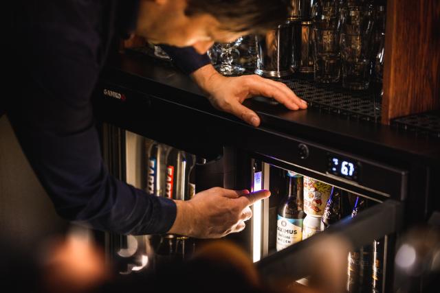 Un barman ouvre une Refroidisseur MG3, révélant des bouteilles magnifiquement illuminées.