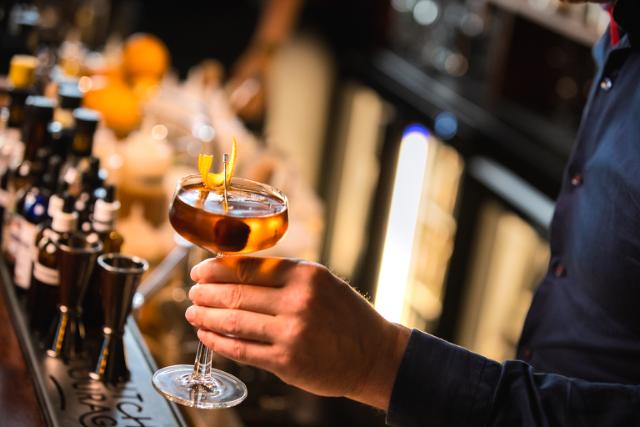 A bartender holds a cocktail in front of a bar