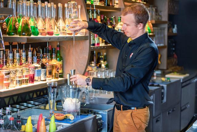 a bartender pours a cocktail in front of a brightly illuminated bar