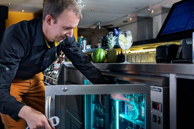 Bartender removes a bottle from a Gamko cooler. A glass containing ice is on top of the cooler along with a pineapple and watermelon.