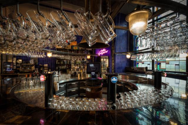 stunning curved bar arrangement fitted with Flexbar drawer units. The surrounding bar area has beer pumps and hanging glasses and there is a neon light in the background.