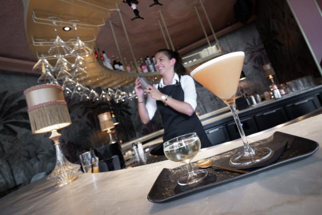 a cocktail is seen in the foreground with a bartender in the background