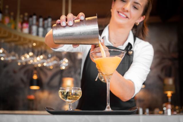 a smiling bartender pours a cocktail